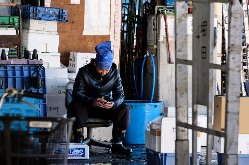 A warehouse employee checking stock information on a smartphone beside storage shelves.