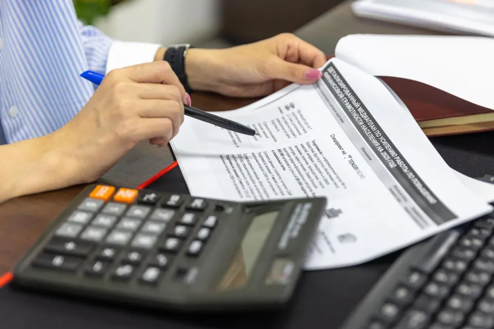 Close-up of a person analyzing financial documents using a calculator and pen.